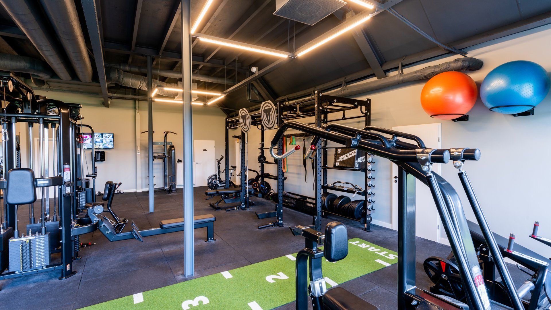 Interieur van een sportschool met fitnessapparatuur en oefenballen aan de muur.