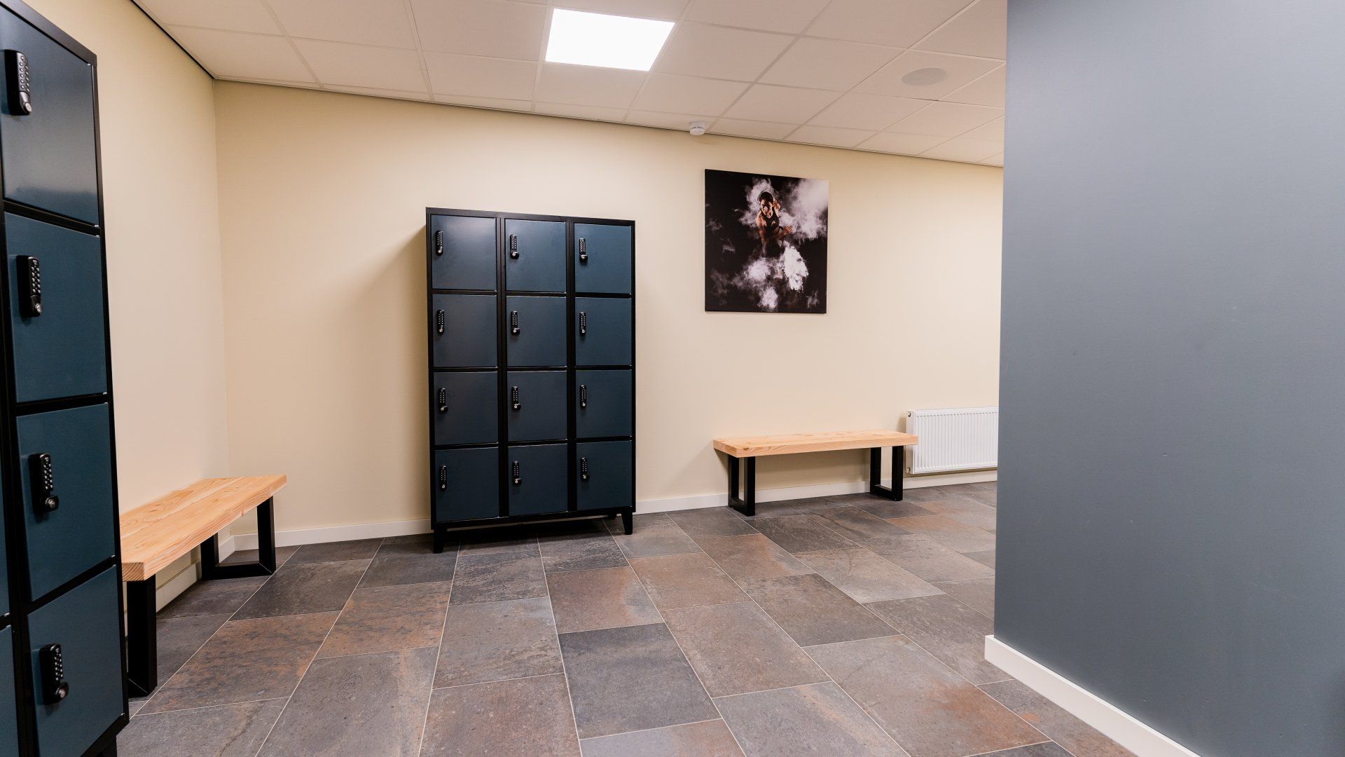 Een kleedkamer met een foto aan de muur en een bankje.
