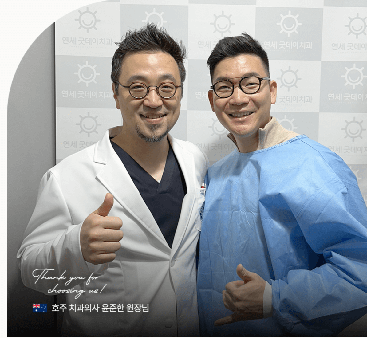 Two smiling men, one in a doctor's coat, the other in surgical scrubs, giving thumbs up. They stand in front of a wall with a logo.