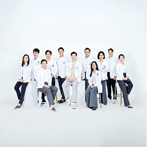 Group of eleven people in white coats and matching outfits posing against a white background. They appear to be health professionals.