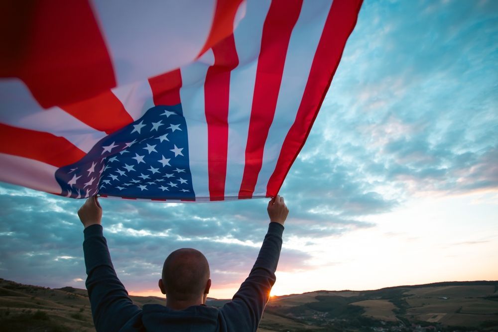 A man is holding an american flag in the air.