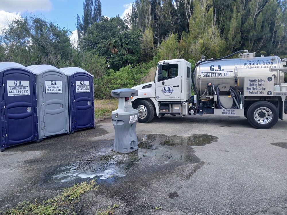 Portable toilets beside a white septic service truck on a wet gravel lot