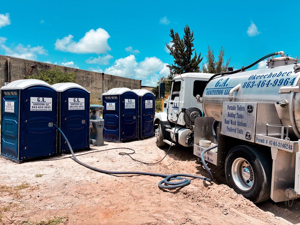 Portable toilets lined up beside a white septic truck in a sunny outdoor lot.