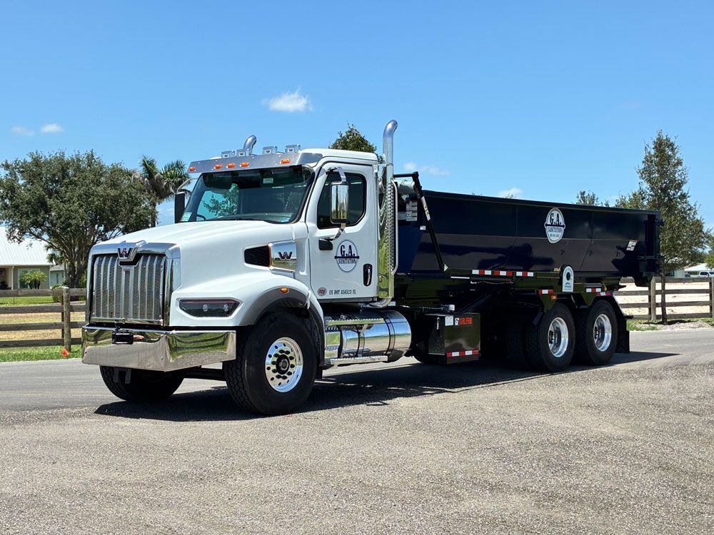 White dump truck parked on a sunny roadside with a black bed and chrome fuel tank.