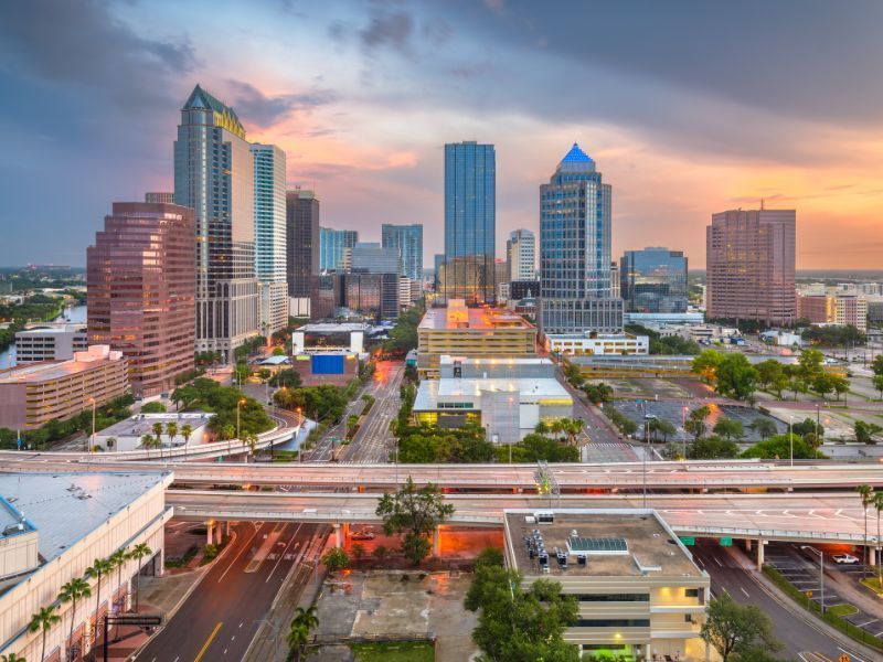 Downtown skyline at sunset with tall office towers, a highway overpass, and city streets below
