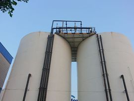 Two large white cylindrical tanks with a metal platform and ladder under a blue sky
