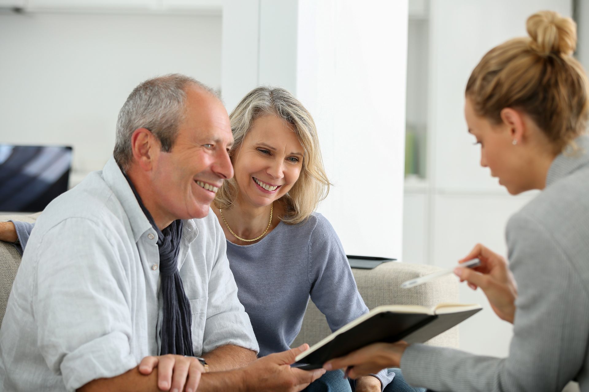 Three people in a bright room look at a book during a conversation.
