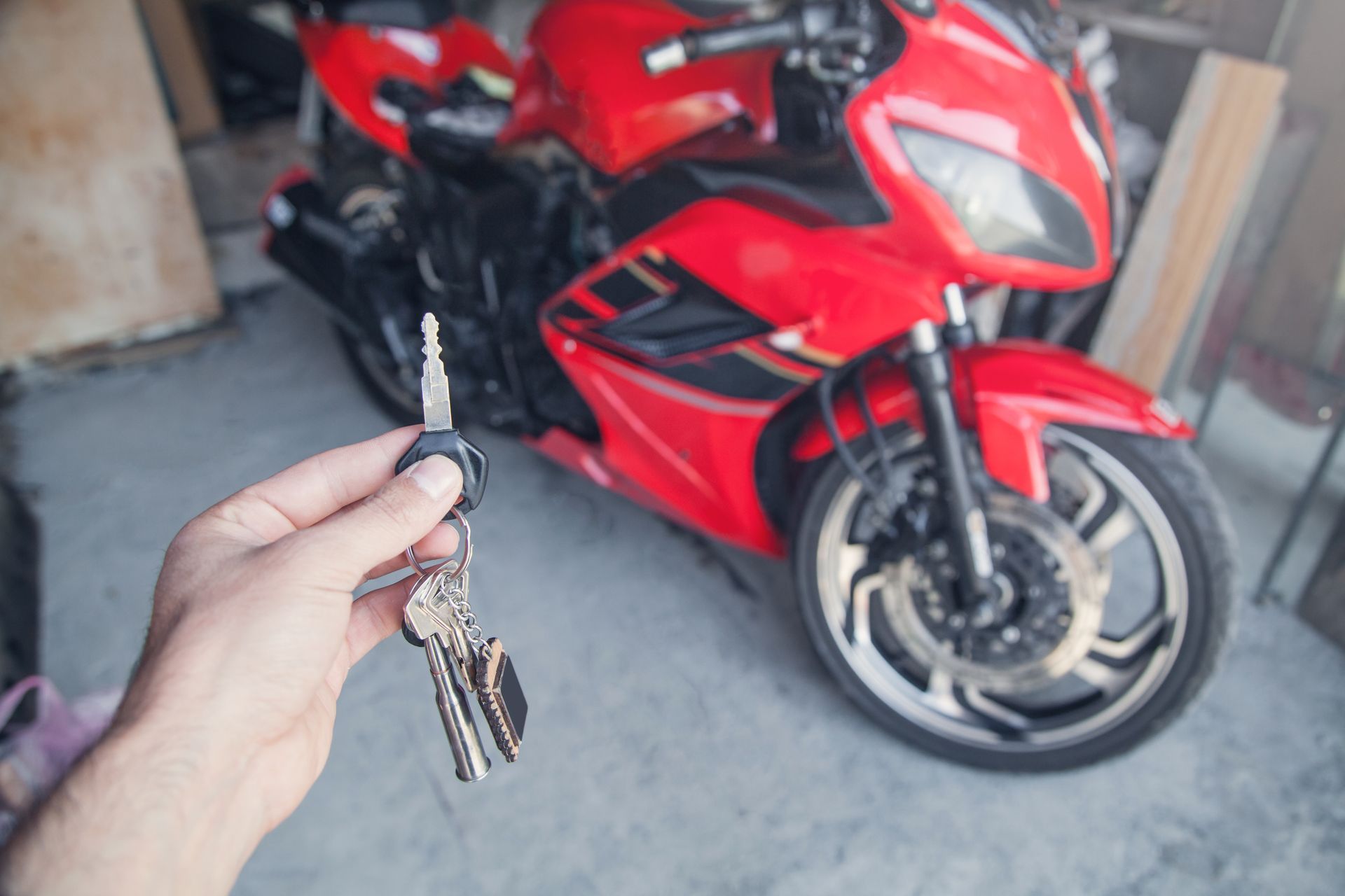 Hand holding motorcycle keys in front of a red sport bike in a garage