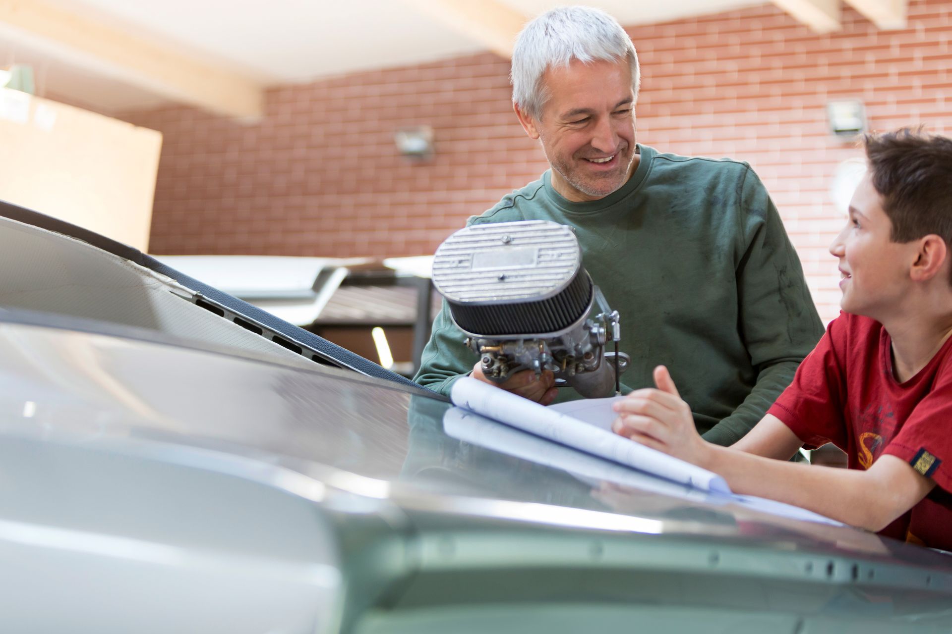 Two people examining a car engine in a garage, with one pointing and the hood open.