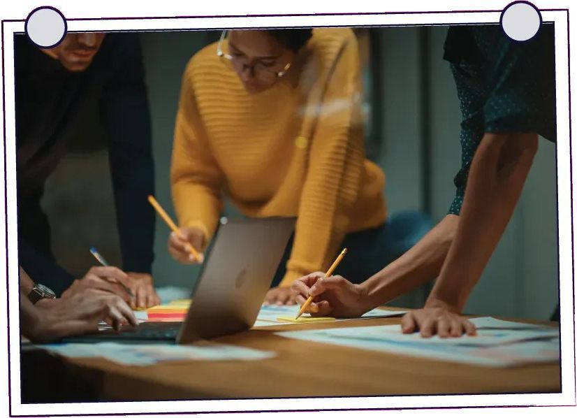 Four people at a table, looking at papers with charts and diagrams. They appear to be discussing a project in an office.