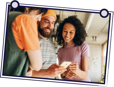 Three people looking at a phone, smiling. Indoors, well-lit.