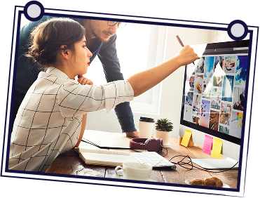 Woman pointing at computer screen with man observing; indoor office setting.