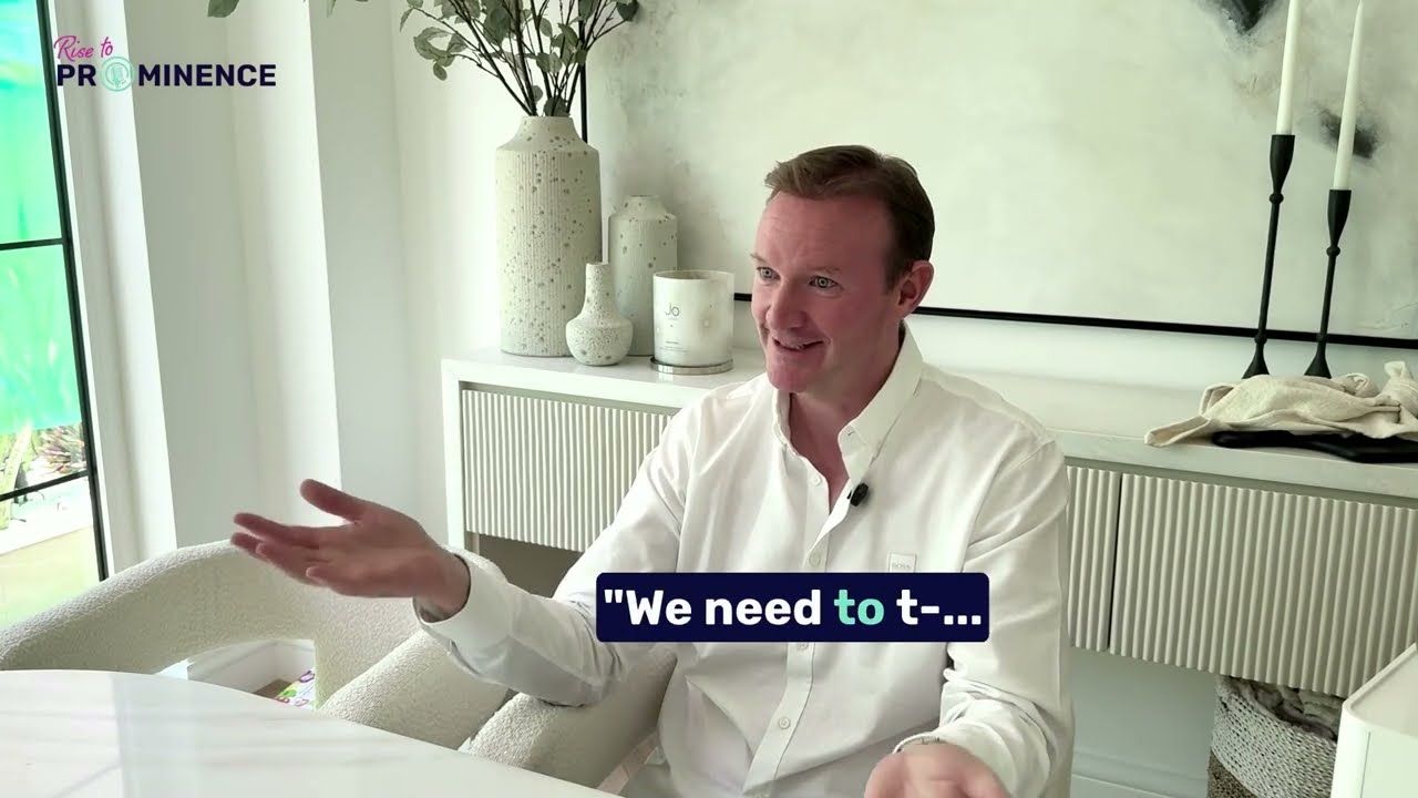 Man in white shirt gestures, talking. White room, plants, and art in the background. Text overlay: "We need to -.."