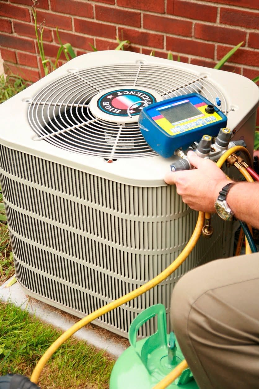 Technician using gauges to service an outdoor air conditioner unit beside a brick wall