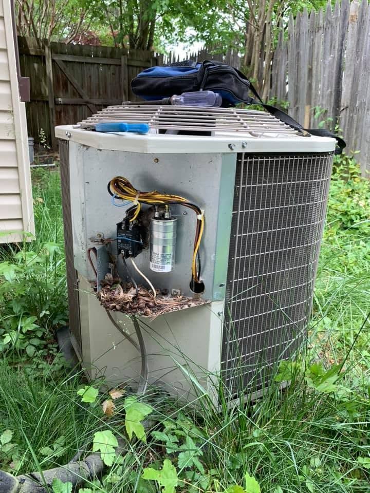 Outdoor HVAC condenser unit with open side panel, exposed wiring, and leaves in a grassy yard.