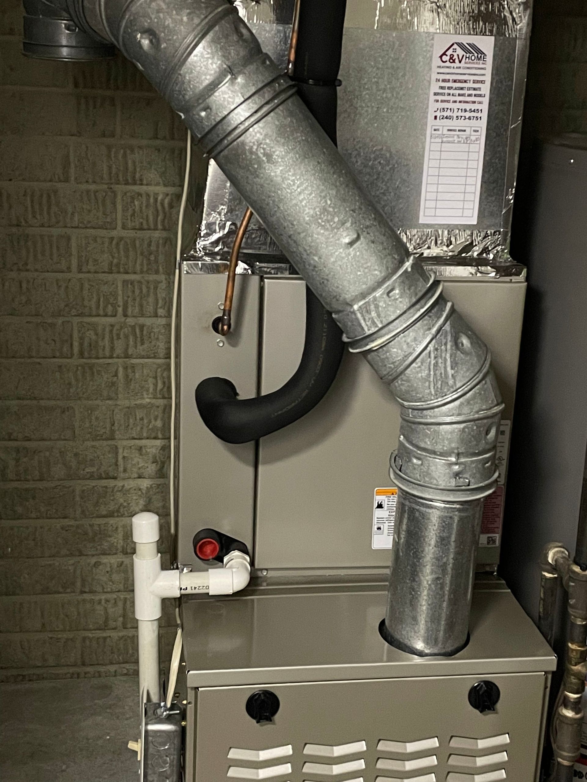 Furnace and ductwork in a utility closet with exposed metal vent pipes and PVC drain lines