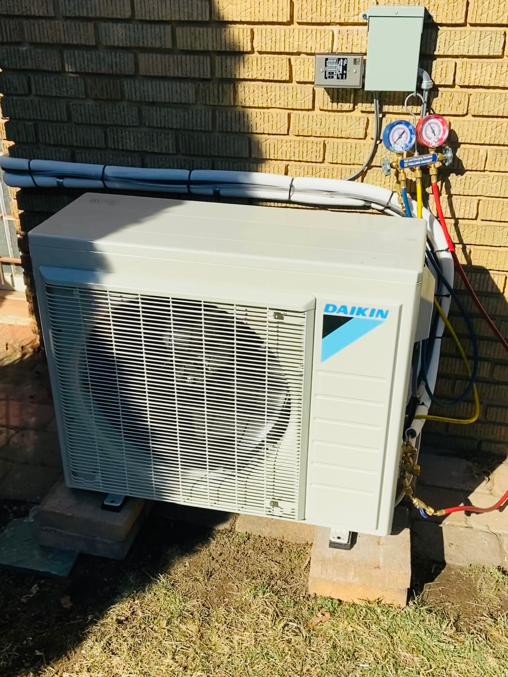 Outdoor air conditioner unit beside a brick wall with pipes and gauges attached