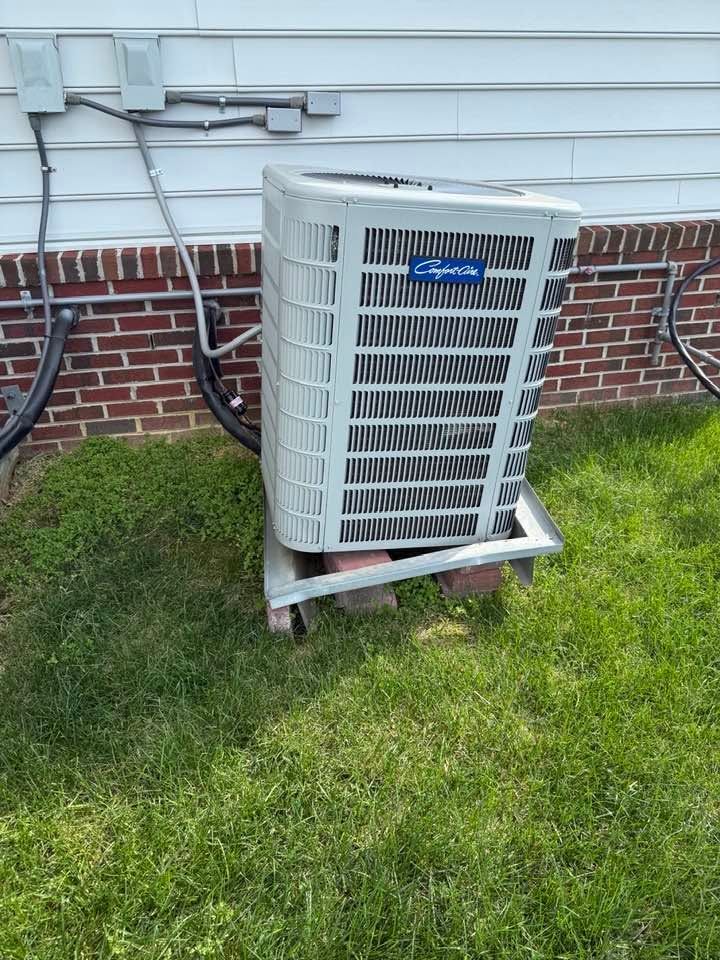 Outdoor HVAC condenser unit beside a brick house wall on a grassy lawn.