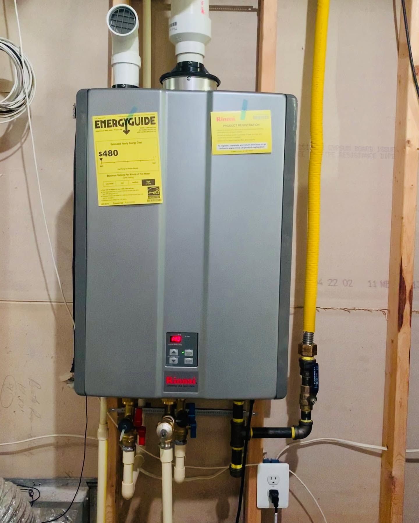 Wall-mounted gray water heater with yellow labels and exposed pipes in a utility room