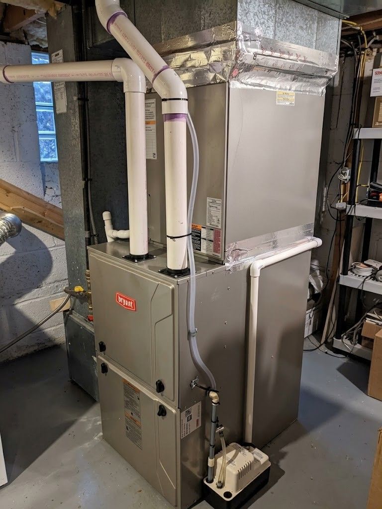 Gray HVAC furnace and ductwork in a basement utility room, with white PVC pipes and a metal cabinet panel.