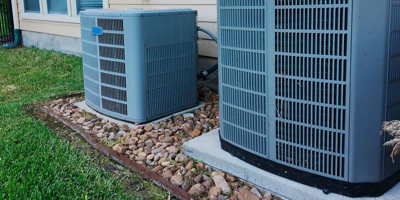 Two outdoor air conditioner units beside a brick house and a grassy lawn