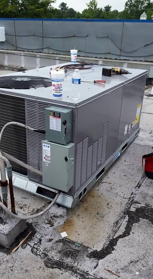 Rooftop HVAC unit with vents and pipes, sitting on a flat roof near a parapet wall.