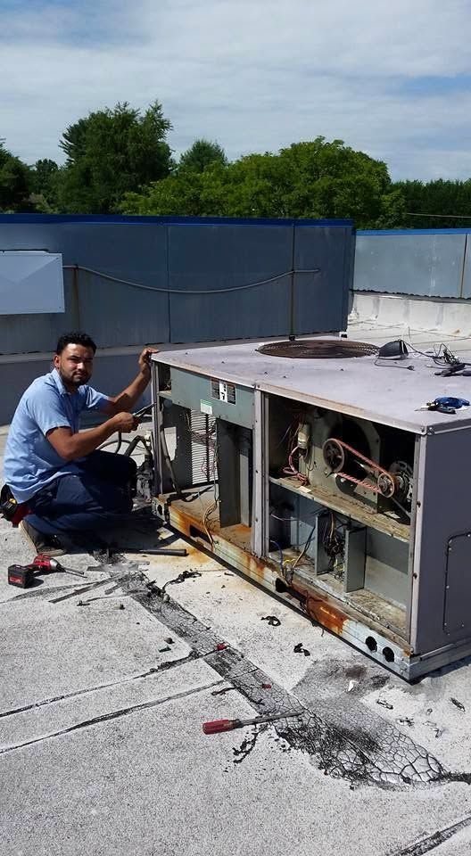 Technician kneeling beside an open rooftop HVAC unit, inspecting wiring and components.