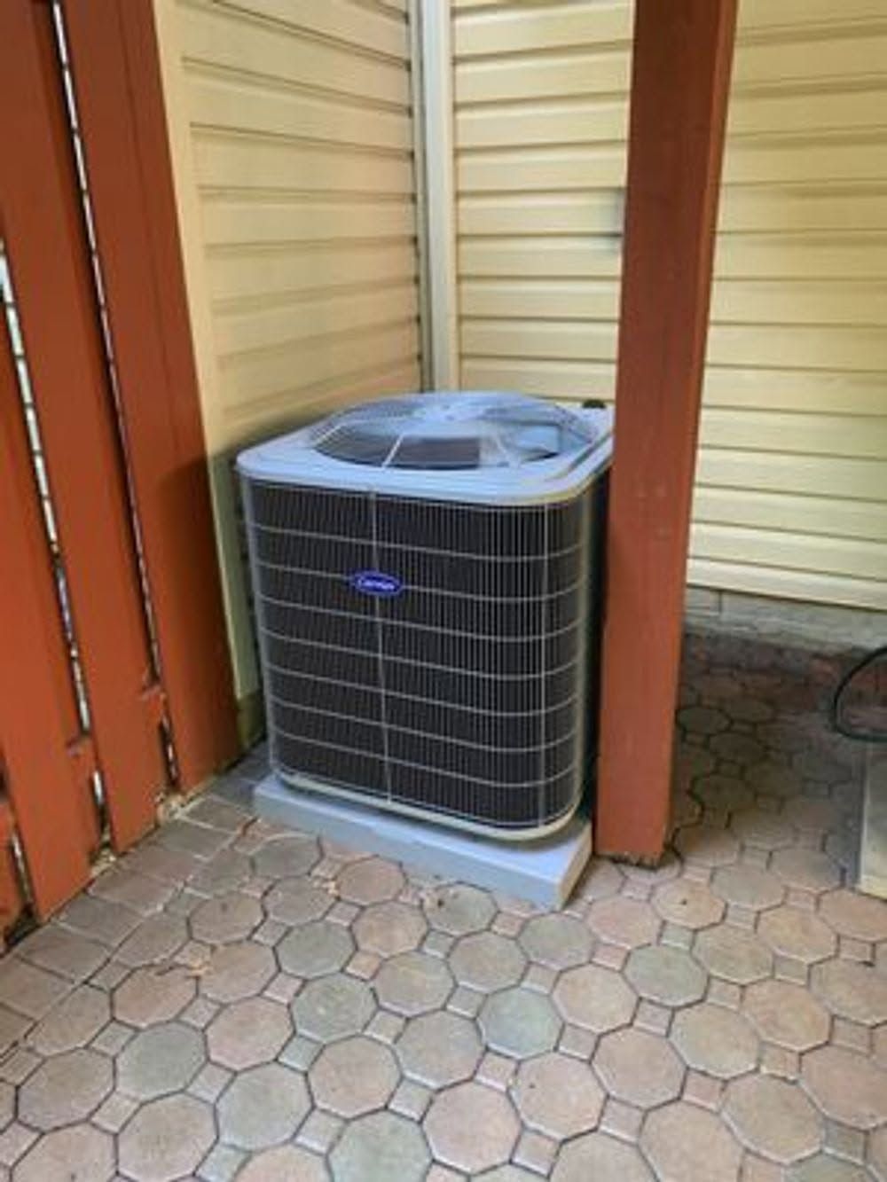 Outdoor air conditioner unit beside a wooden fence on a tiled patio
