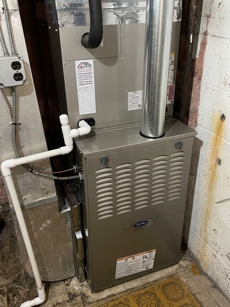 Furnace with metal vent pipes and white PVC drain line in a basement utility area