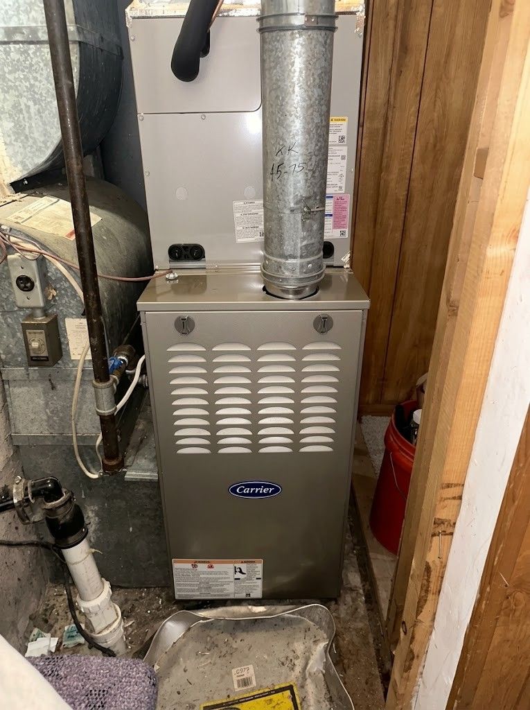 Basement furnace and HVAC unit with metal ductwork and pipes in a narrow utility space.