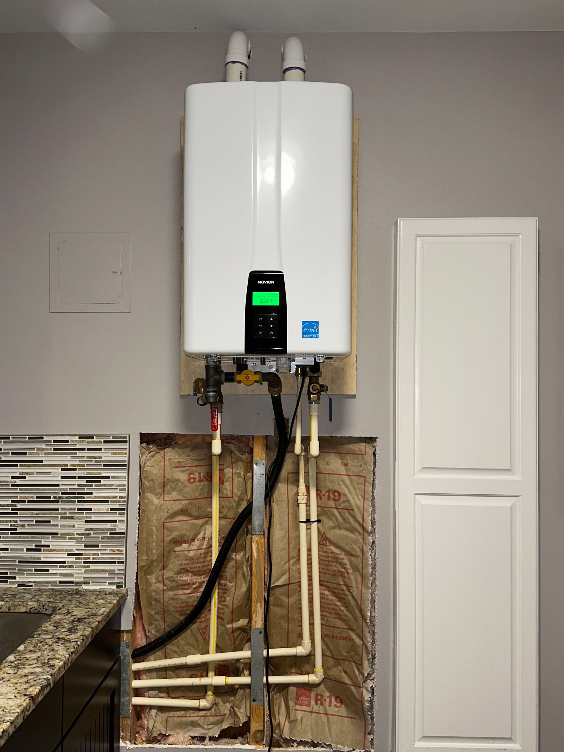 Wall-mounted white tankless water heater with exposed pipes in a utility area.