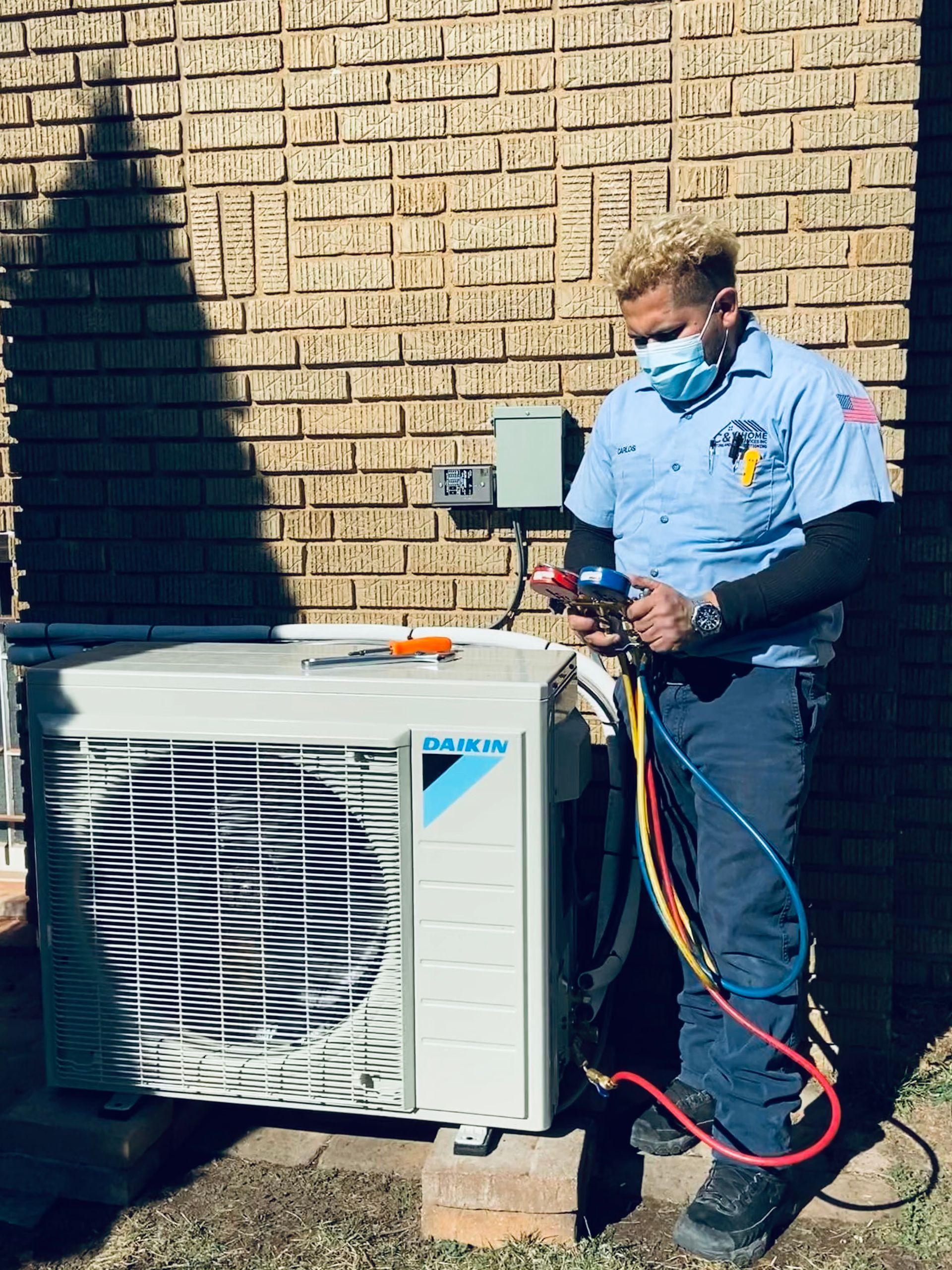 Technician in blue uniform servicing an outdoor HVAC unit beside a brick wall