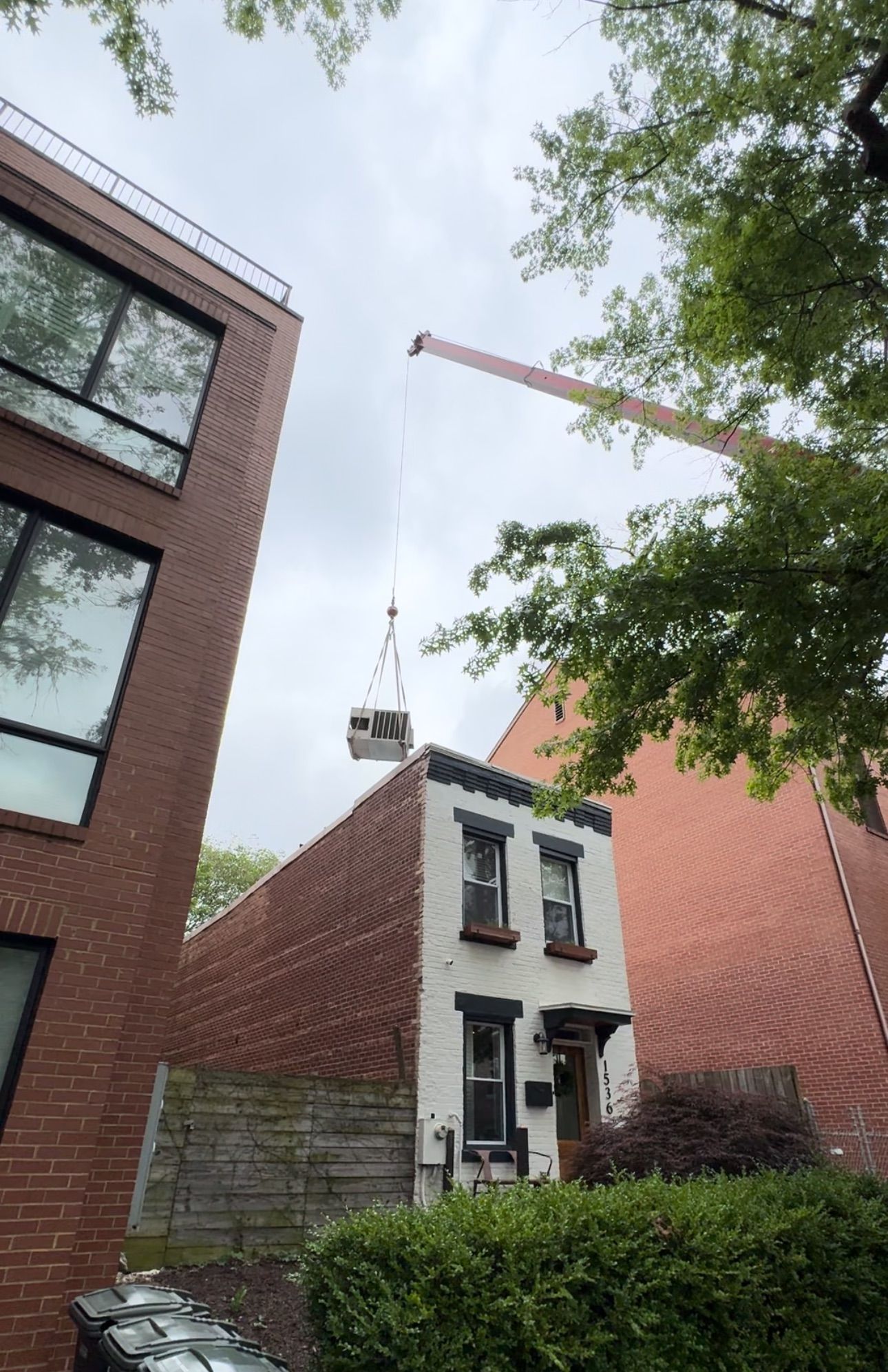 Crane lifting a small house section above brick homes in a narrow urban courtyard