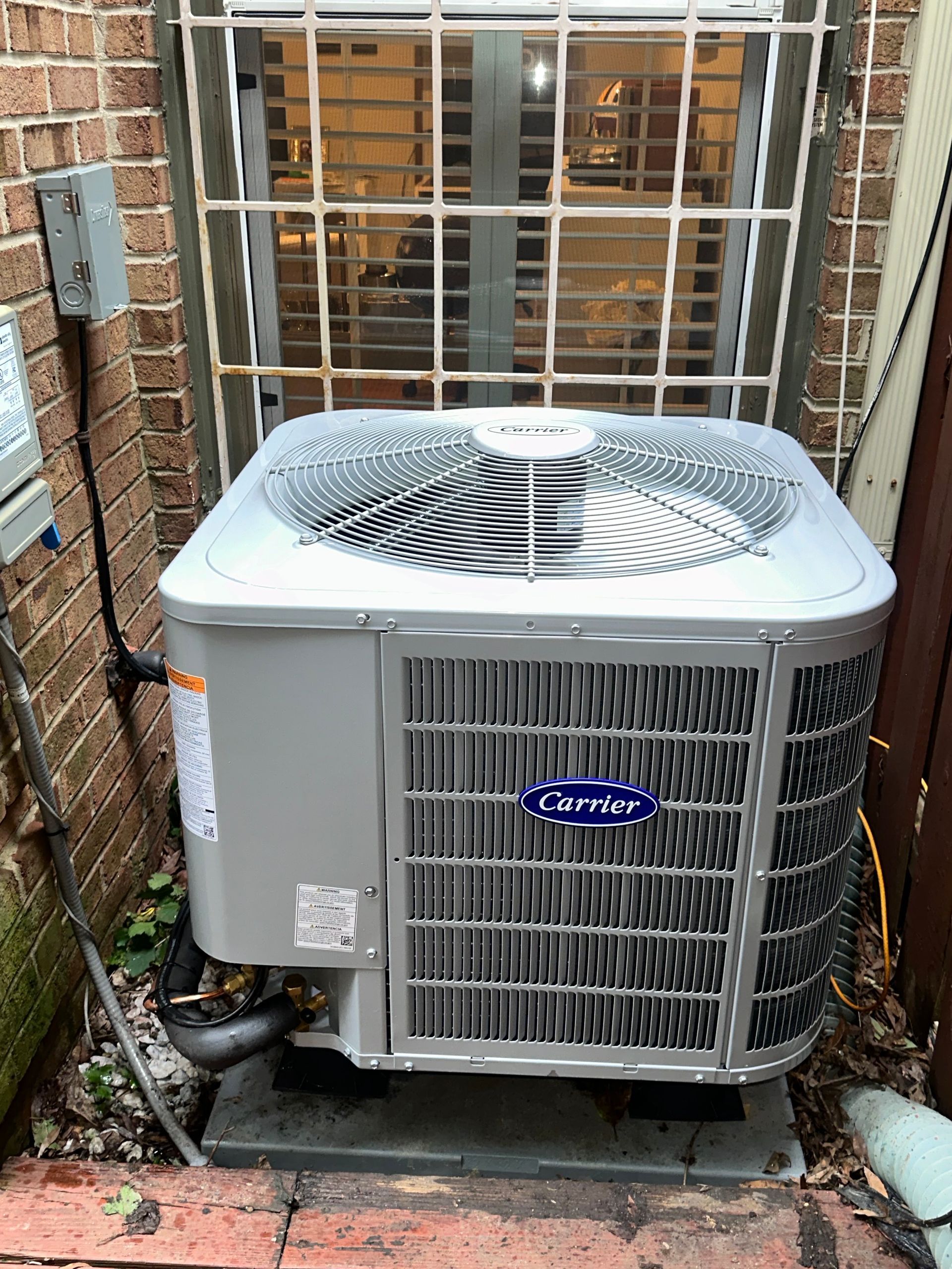Outdoor Carrier air conditioner unit beside a brick building and metal fence in a narrow alley