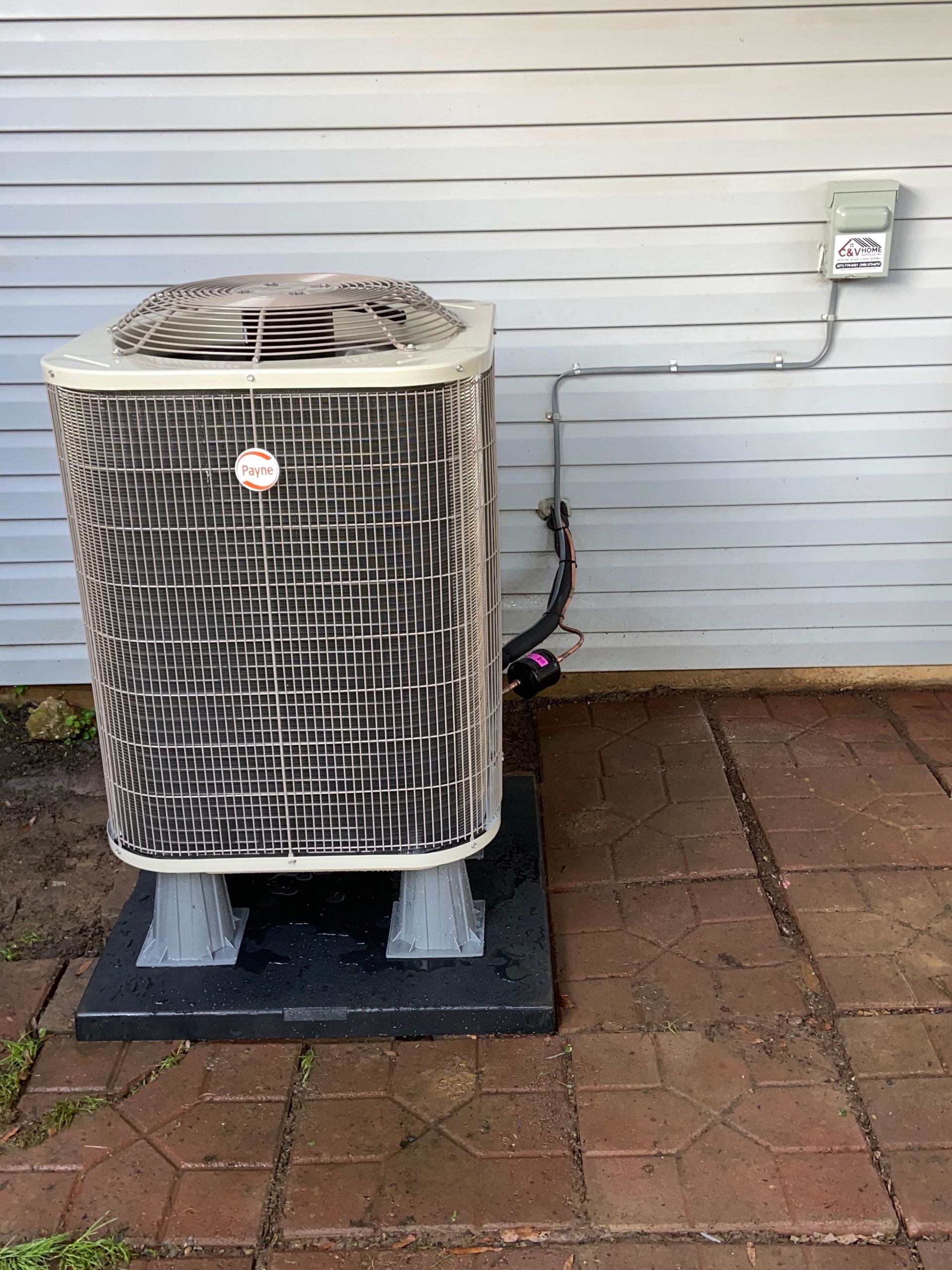 Outdoor air conditioner unit beside a house wall on a brick patio