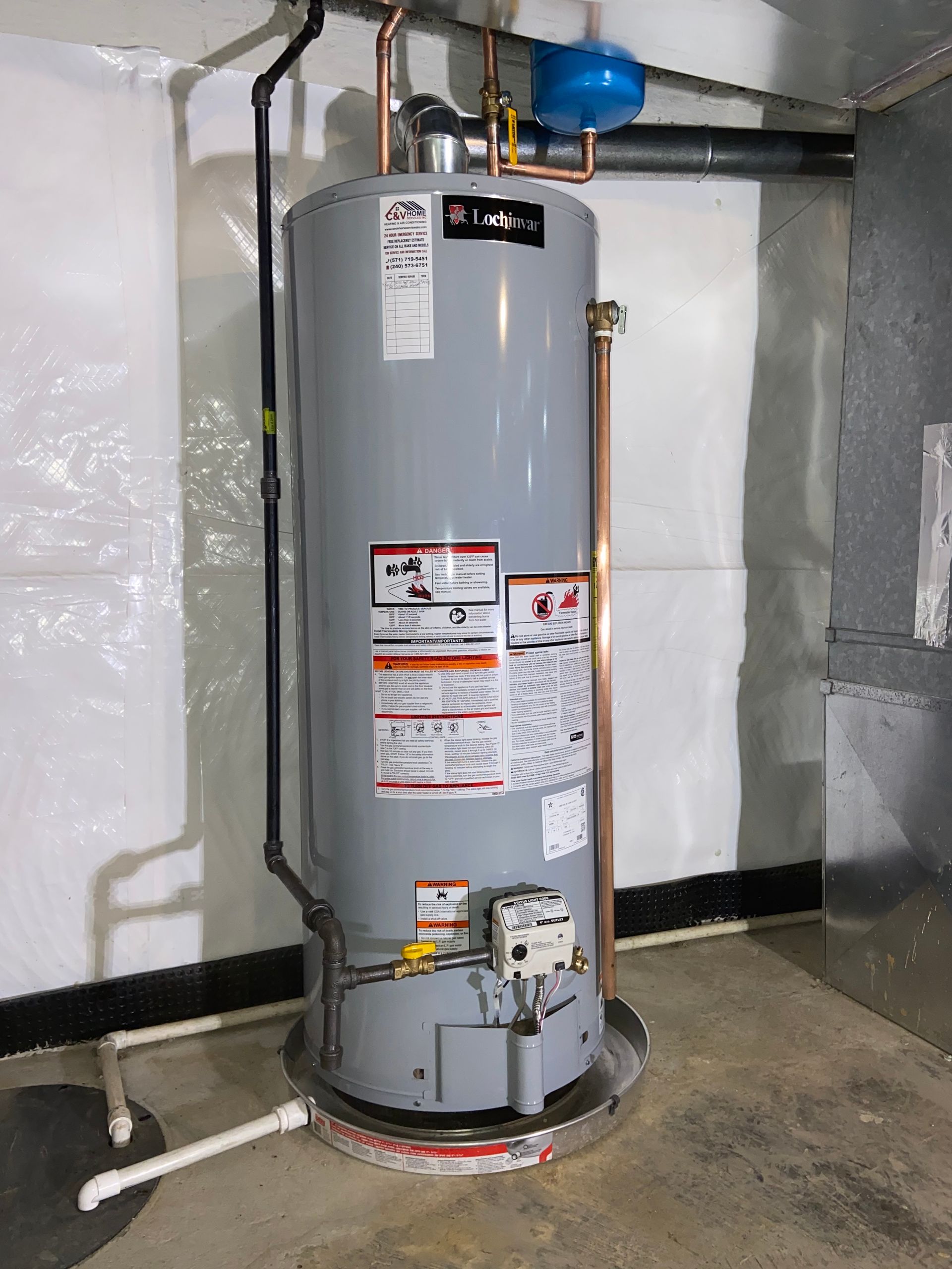 Gray water heater in a utility room with exposed pipes and a red base ring