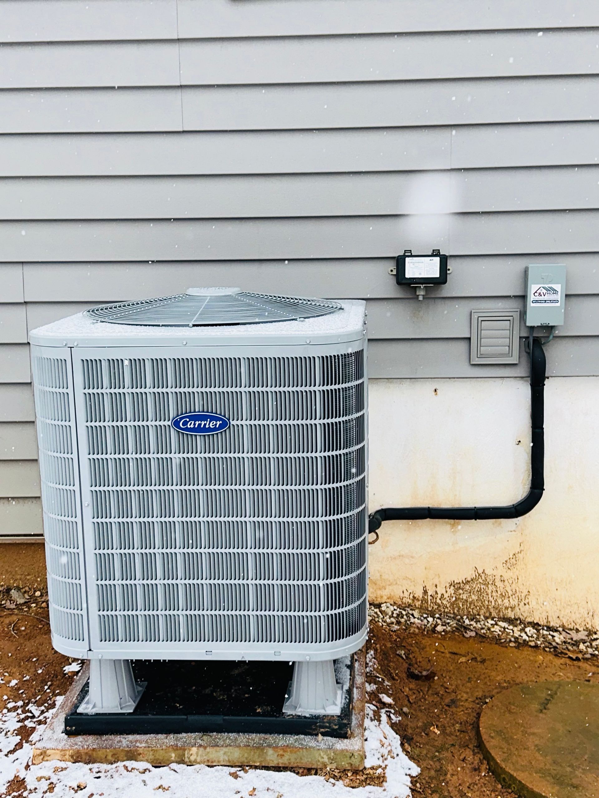Outdoor air conditioner unit beside a house wall with visible rust stains and electrical conduit nearby