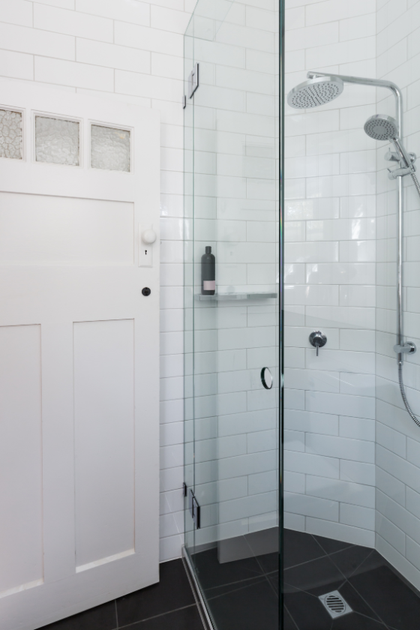 A bathroom with white tiles and a walk in shower with a glass door.