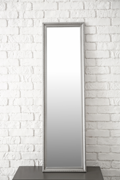 A full length mirror is hanging on a white brick wall.