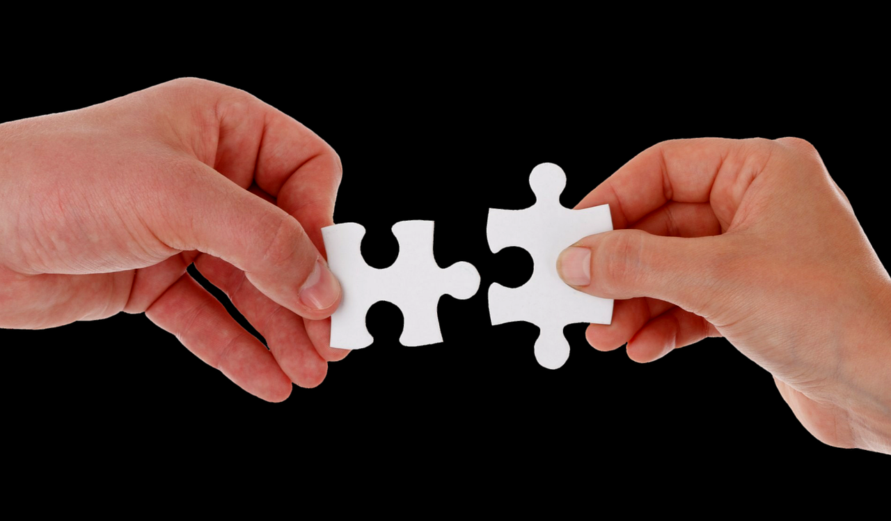 Twee handen houden puzzelstukjes vast en proberen ze tegen een zwarte achtergrond met elkaar te verbinden.