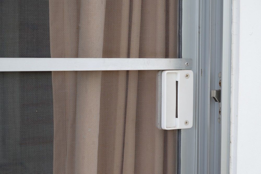 Close-up of a white screen door latch. Beige curtains are visible behind the screen. — Kincumber Glass & Glazing in Kincumber, NSW