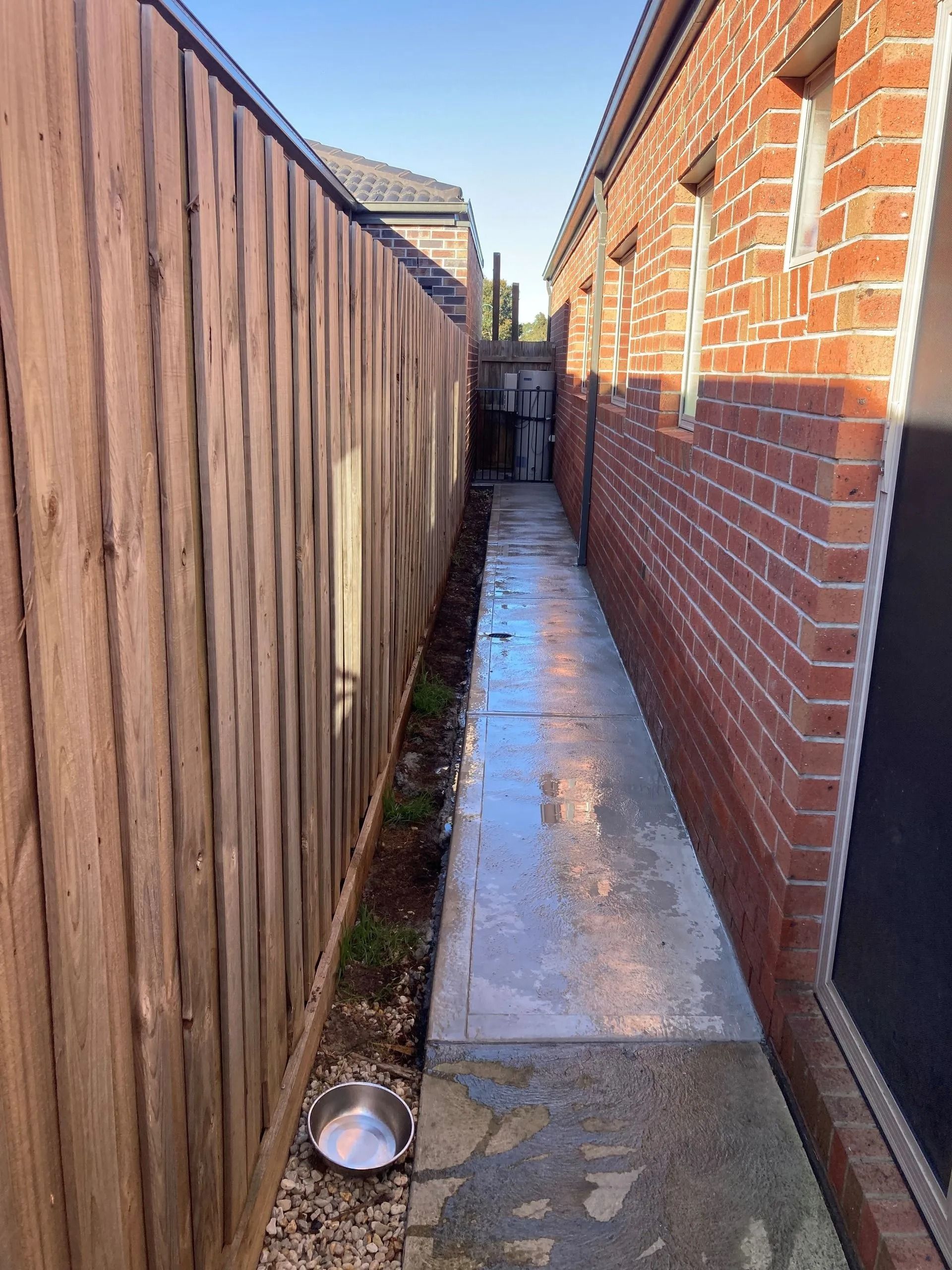 Narrow concrete walkway between a wooden fence and a brick wall.