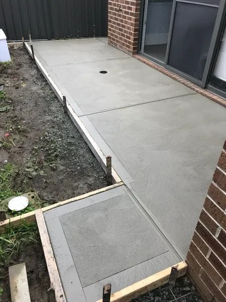 Freshly poured concrete patio with wooden framing next to a brick wall and sliding glass door.