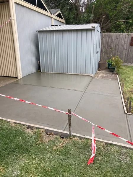 New concrete patio with a small shed and safety tape in a backyard.
