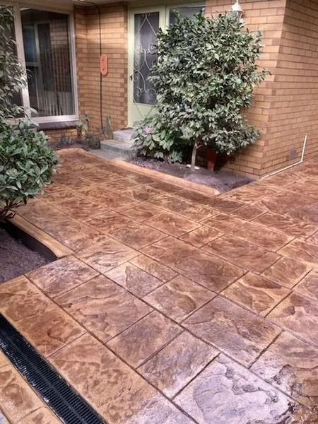 Stamped concrete patio with brown and gray tones, leading to a home entrance with green plants.