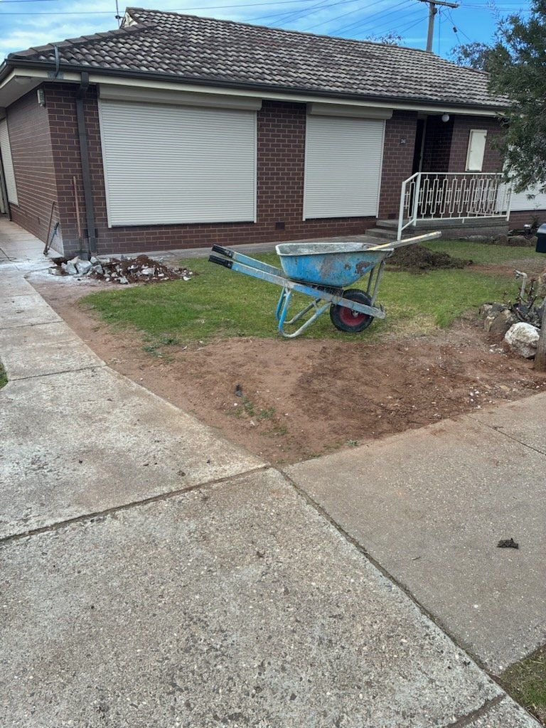House with closed shutters, lawn with a wheelbarrow, and sidewalk.