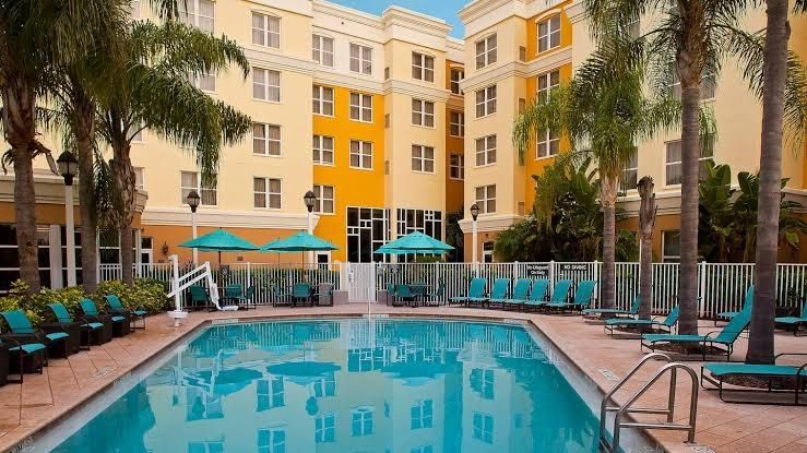 A large swimming pool surrounded by chairs and umbrellas in front of a hotel.