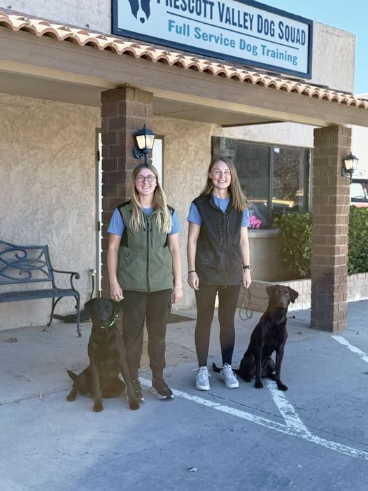 two people with two dogs on leashes outside a dog training facility