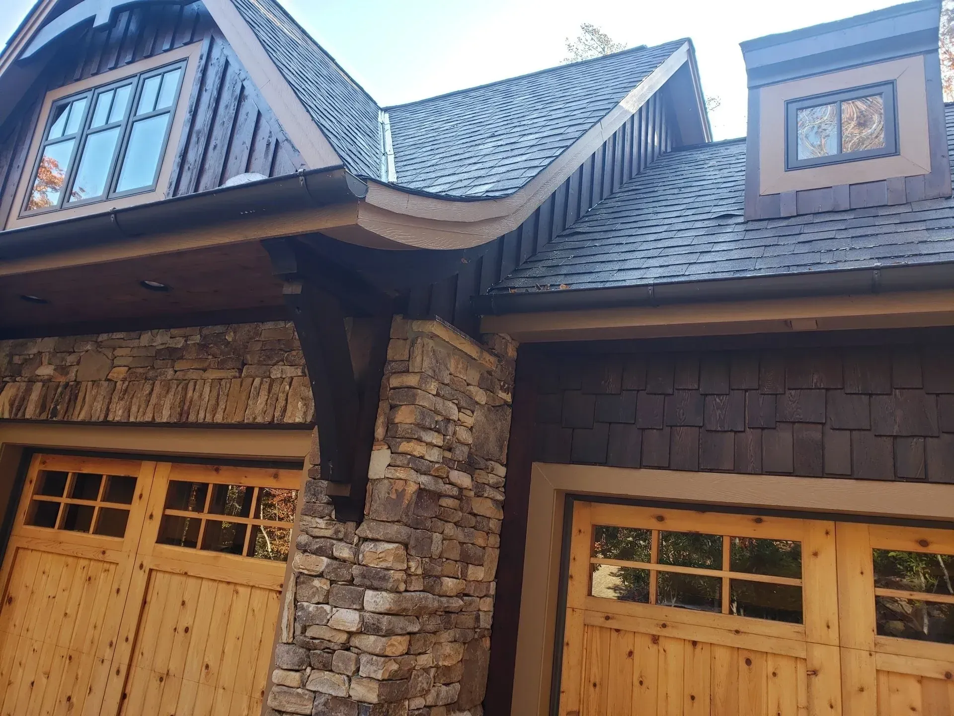 A house with two wooden garage doors and a stone wall.