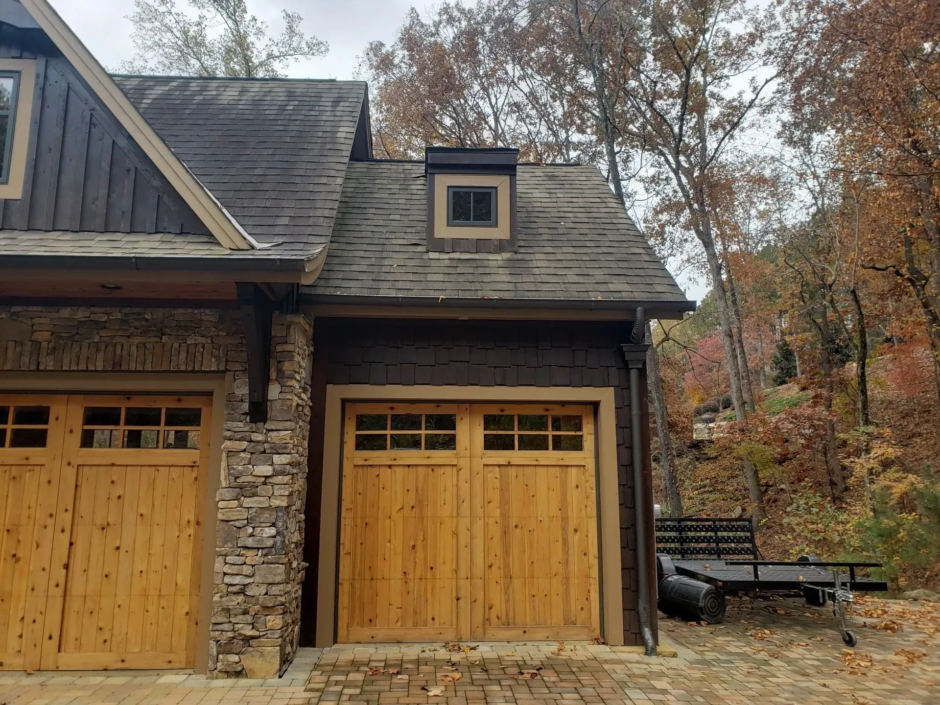 A house with two wooden garage doors and a trailer parked in front of it.